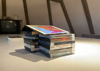 Ein Tablet auf einem Stapel DVDs, im Hintergrund ein Buch und ein Fernseher ©Stadtbibliothek 